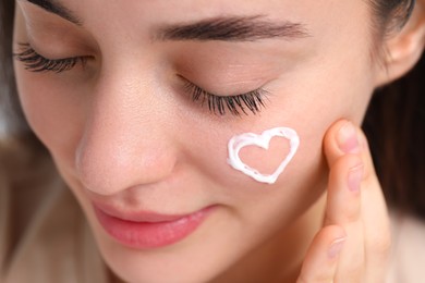 Photo of Young woman with dry skin and heart made of cream on her face, closeup