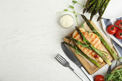 Photo of Tasty grilled chicken fillet served with asparagus and sprouts on white wooden table, flat lay. Space for text