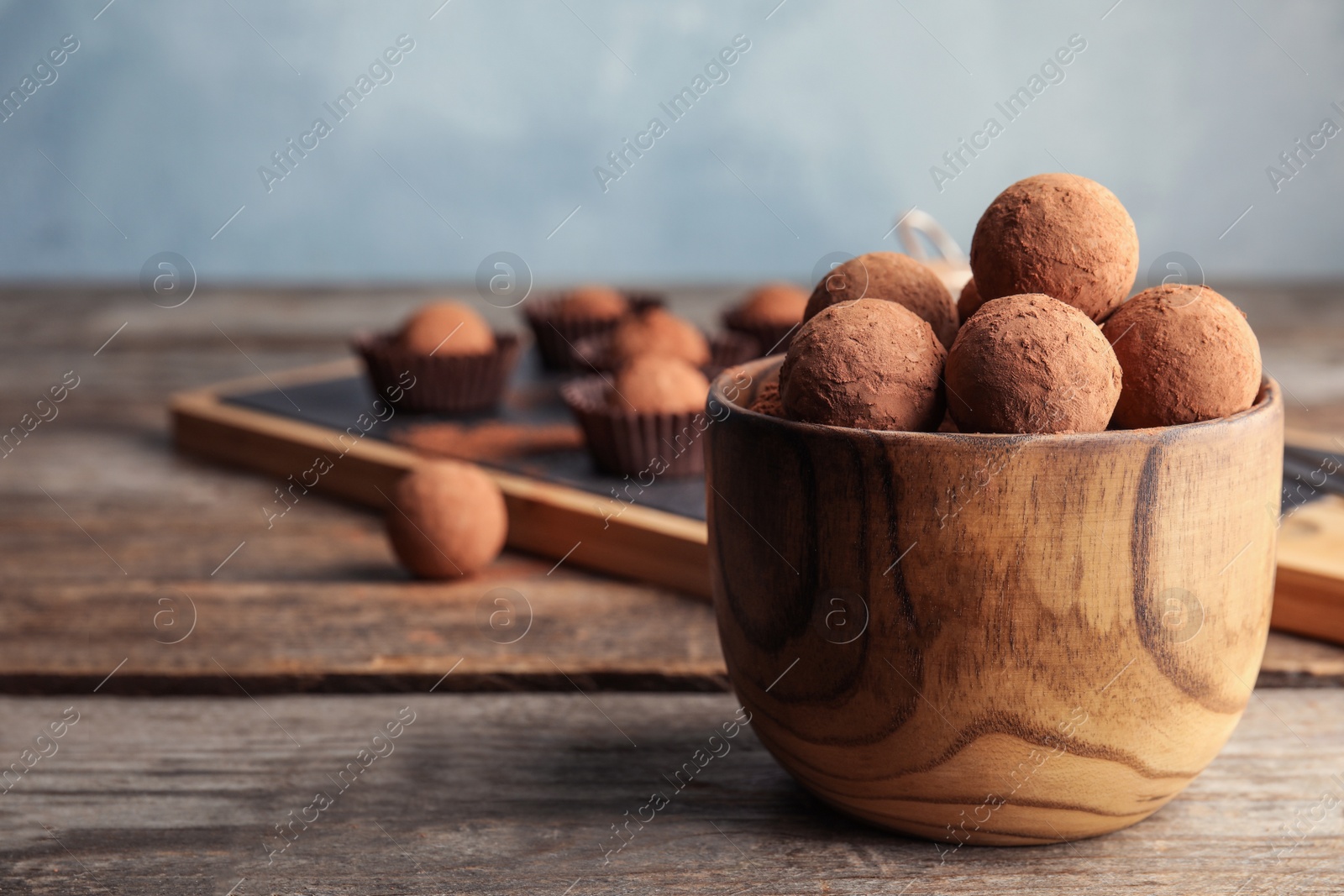 Photo of Bowl with chocolate truffles on wooden table, space for text