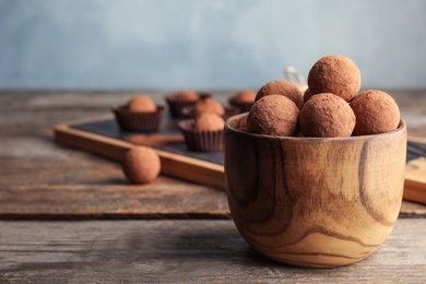 Photo of Bowl with chocolate truffles on wooden table, space for text