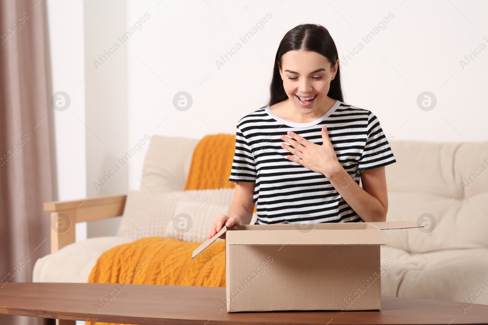 Photo of Emotional young woman opening parcel at home. Internet shopping