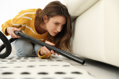 Photo of Young woman using vacuum cleaner at home