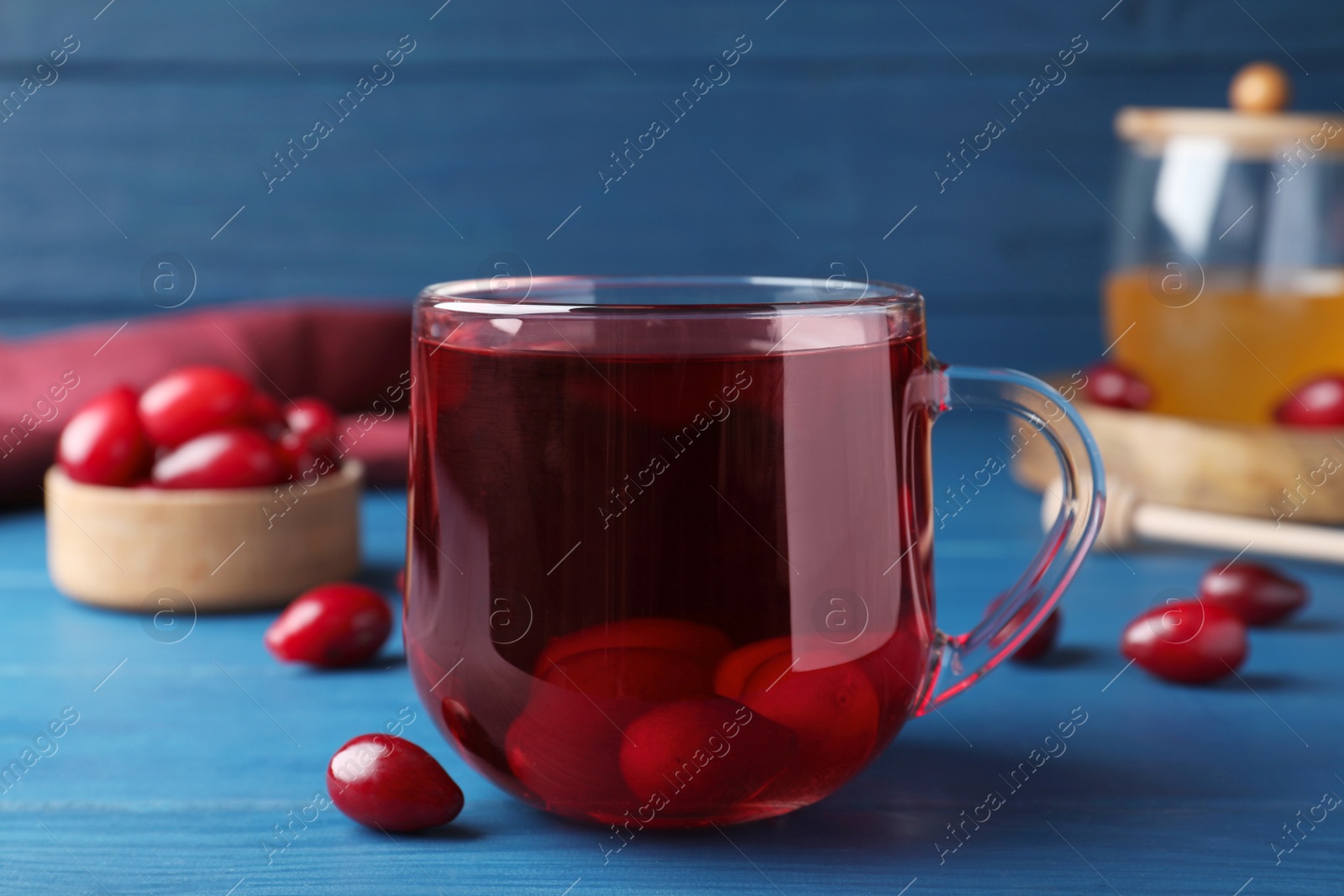 Photo of Glass cup of fresh dogwood tea with berries on blue wooden table
