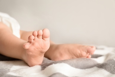 Photo of Little baby with cute feet on bed against light background, closeup. Space for text