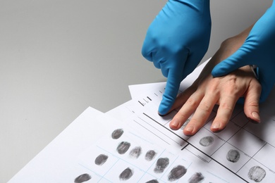 Photo of Investigator taking fingerprints of suspect on grey table, closeup. Space for text