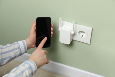 Woman using smartphone for wireless Wi-Fi repeater indoors, closeup