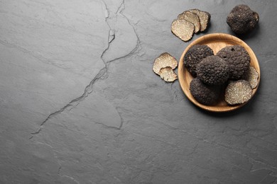 Photo of Black truffles with wooden plate on grey table, flat lay. Space for text