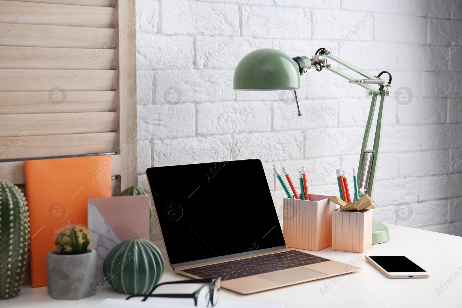 Photo of Modern workplace with laptop on table against brick wall. Mockup for design