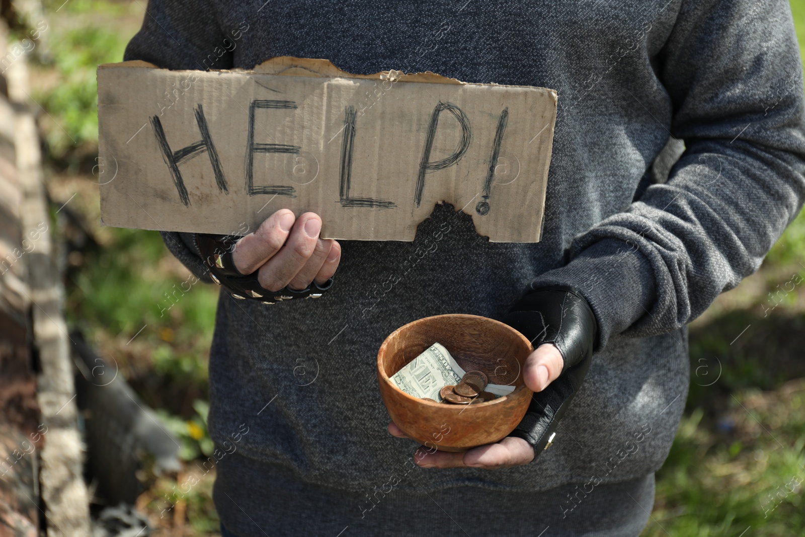 Photo of Poor homeless man holding help sign and bowl with donations outdoors, closeup