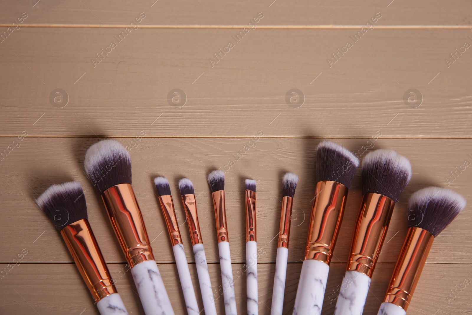 Photo of Set of professional makeup brushes on wooden background, above view. Space for text