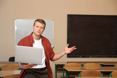 Portrait of male teacher with laptop in modern classroom