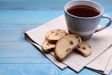 Photo of Sweet hard chuck crackers with raisins and cup of tea on light blue wooden table. Space for text