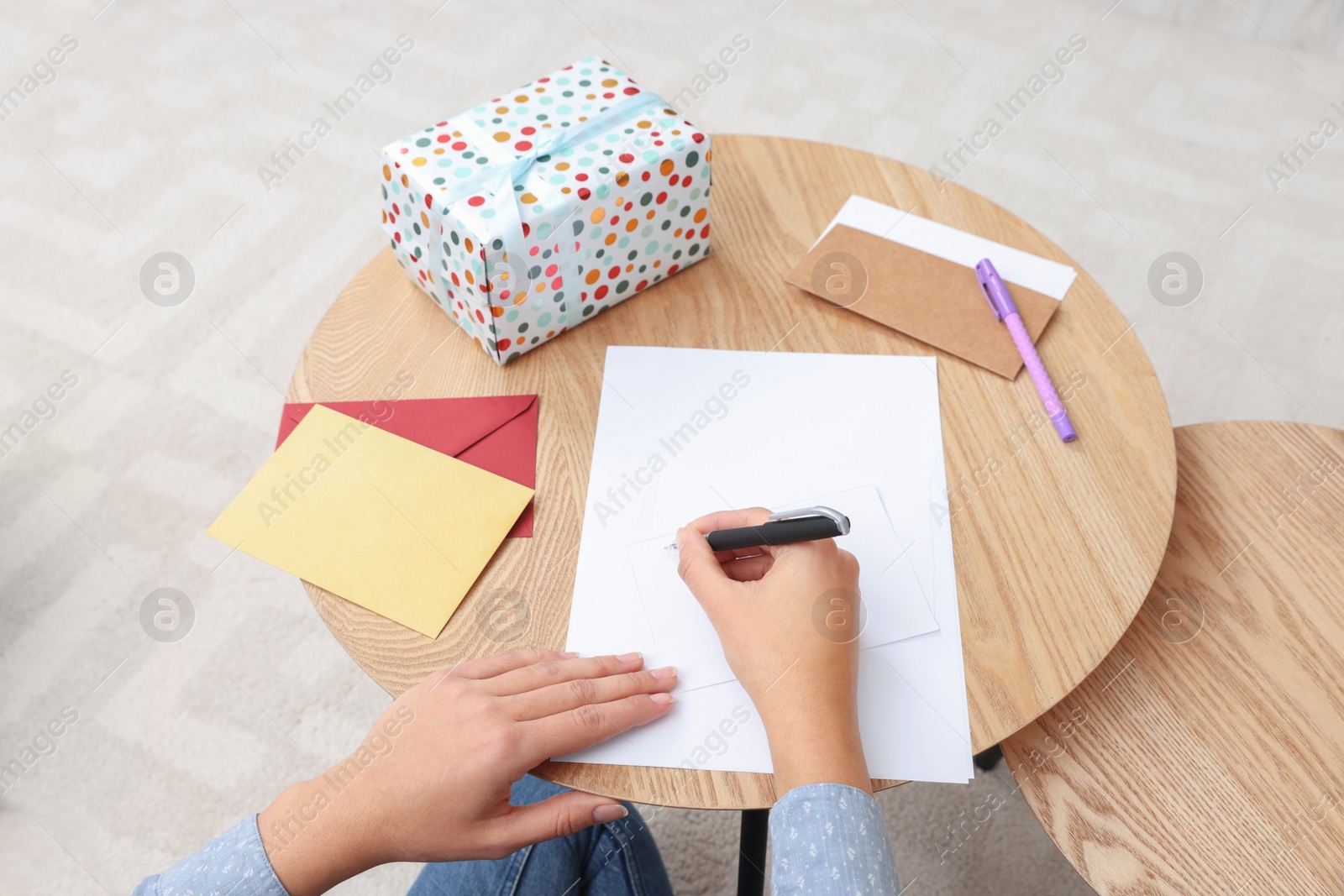 Photo of Young woman writing message in greeting card at wooden table indoors, above view