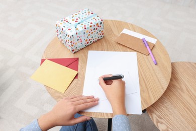 Photo of Young woman writing message in greeting card at wooden table indoors, above view