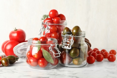 Photo of Pickling jars with fresh ripe tomatoes on white marble table