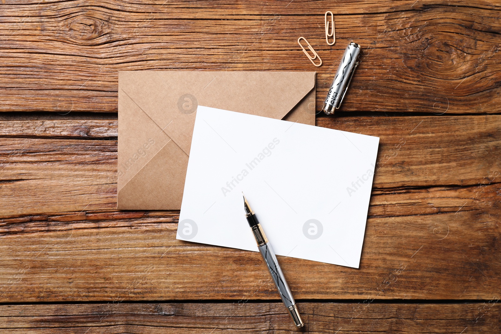 Photo of Blank sheet of paper, pen, paperclips and letter envelope on wooden table, flat lay. Space for text