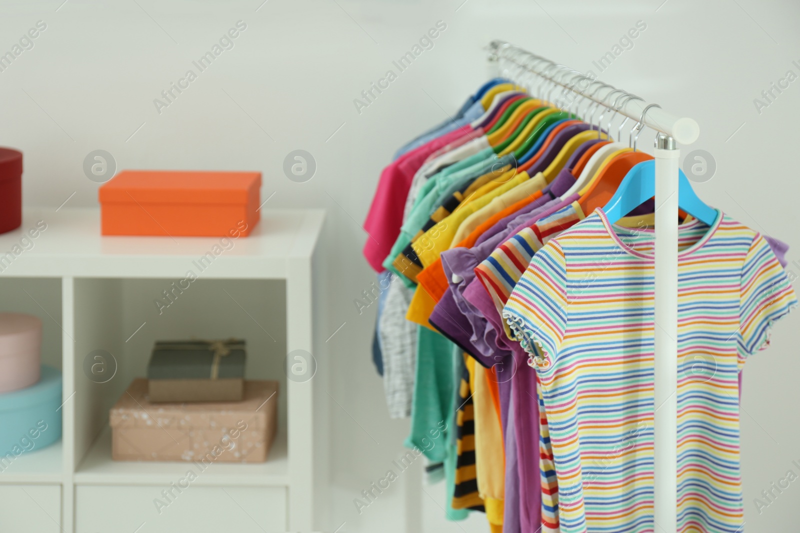 Photo of Different child's clothes hanging on rack indoors. Space for text