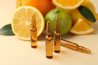 Skincare ampoules with vitamin C, different citrus fruits and leaves on beige background, closeup