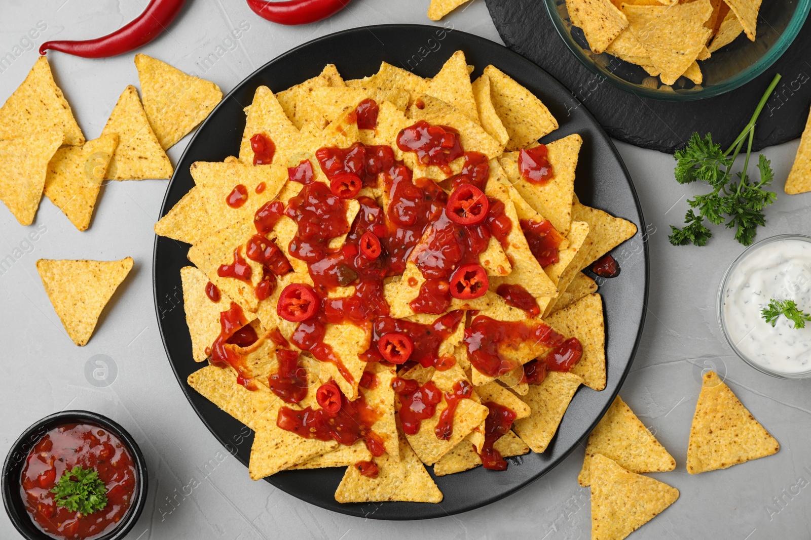 Photo of Mexican nacho chips with different sauces on grey table, flat lay