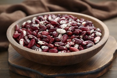 Photo of Bowl with dry kidney beans on wooden board, closeup