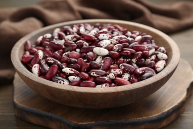 Bowl with dry kidney beans on wooden board, closeup