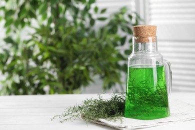 Jug of homemade refreshing tarragon drink and sprigs on white wooden table, space for text