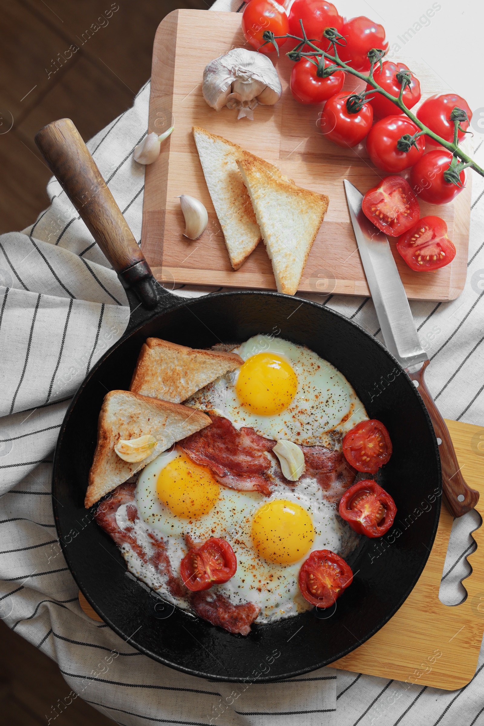 Photo of Delicious fried eggs with bacon and tomatoes in pan on table, flat lay