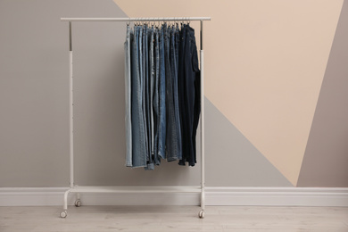 Photo of Rack with stylish jeans near color wall. Space for text