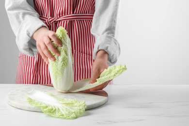 Photo of Woman separating leaf from fresh chinese cabbage at white marble table, space for text