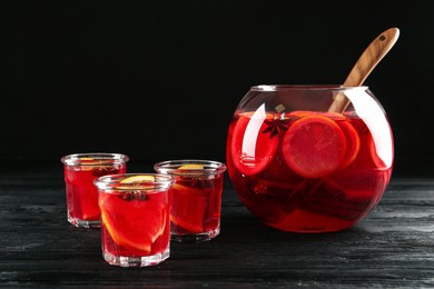 Photo of Bowl and glasses of delicious aromatic punch drink on black wooden table