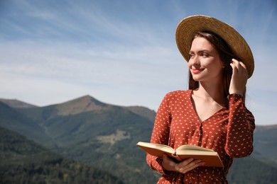 Beautiful young woman reading book in mountains, space for text