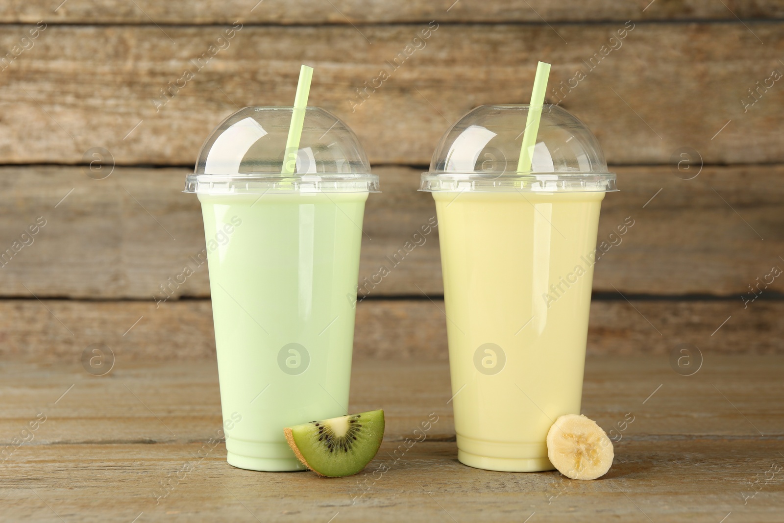 Photo of Plastic cups with different tasty smoothies and fresh fruits on wooden table