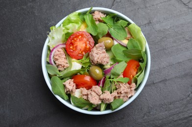 Photo of Bowl of delicious salad with canned tuna and vegetables on black table, top view