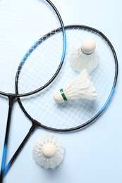 Photo of Feather badminton shuttlecocks and rackets on light blue background, flat lay