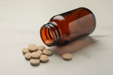 Photo of Overturned bottle with dietary supplement pills on white table