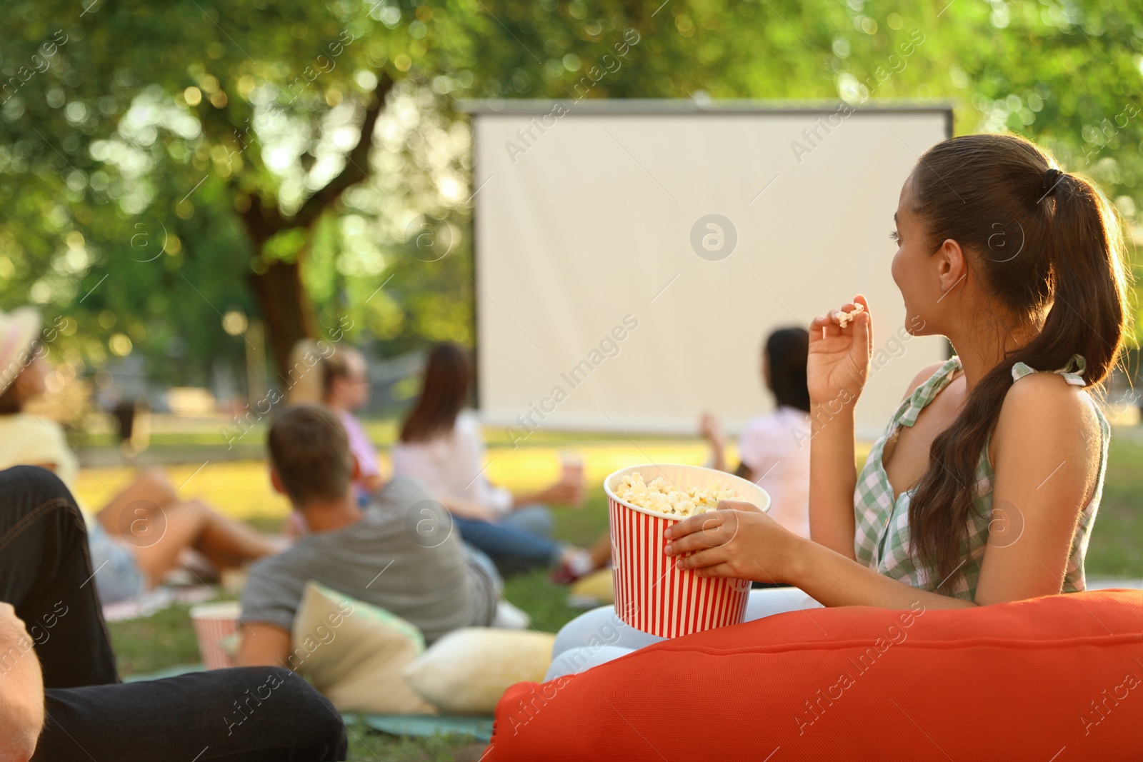 Photo of Young woman with popcorn watching movie in open air cinema. Space for text