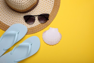 Photo of Stylish white flip flops, sunglasses, hat and seashell on yellow background, flat lay. Space for text