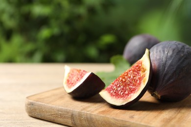 Photo of Whole and cut ripe figs on wooden table against blurred green background, closeup. Space for text