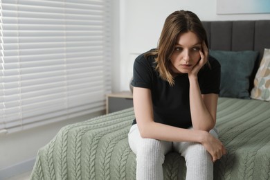 Photo of Sad young woman sitting on bed at home, space for text
