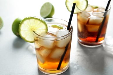 Glasses of cocktail with cola, ice and cut lime on light background