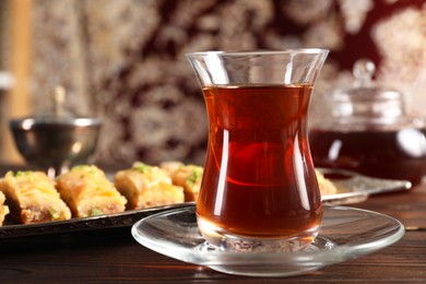 Photo of Traditional Turkish tea in glass and fresh baklava on wooden table, closeup