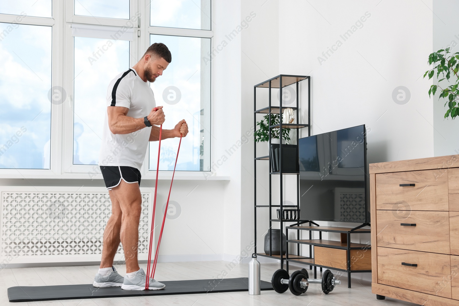 Photo of Athletic man doing exercise with elastic resistance band on mat at home