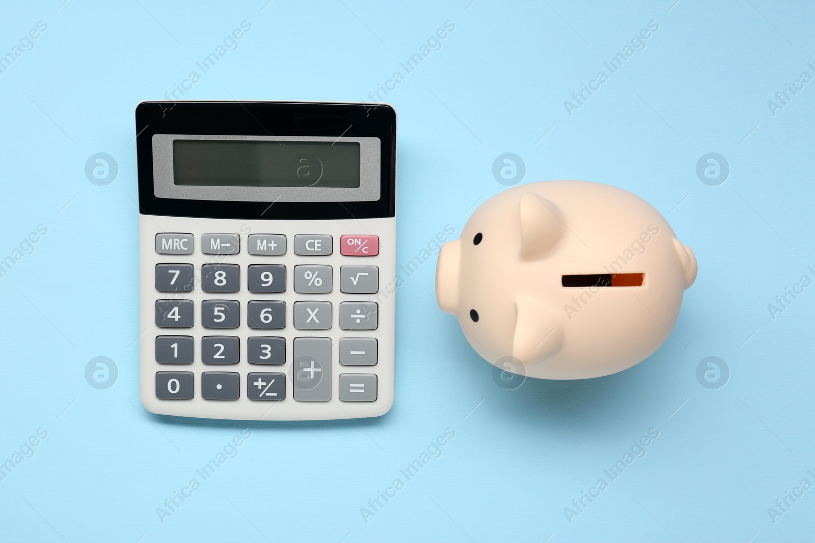 Photo of Calculator and piggy bank on light blue background, top view