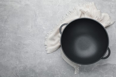 Photo of Empty iron wok and towel on grey table, top view. Space for text