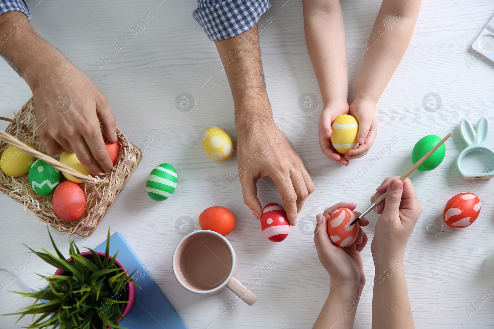 Photo of Father, mother and their child painting Easter eggs on wooden background, top view