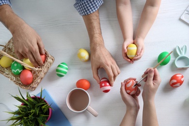 Photo of Father, mother and their child painting Easter eggs on wooden background, top view