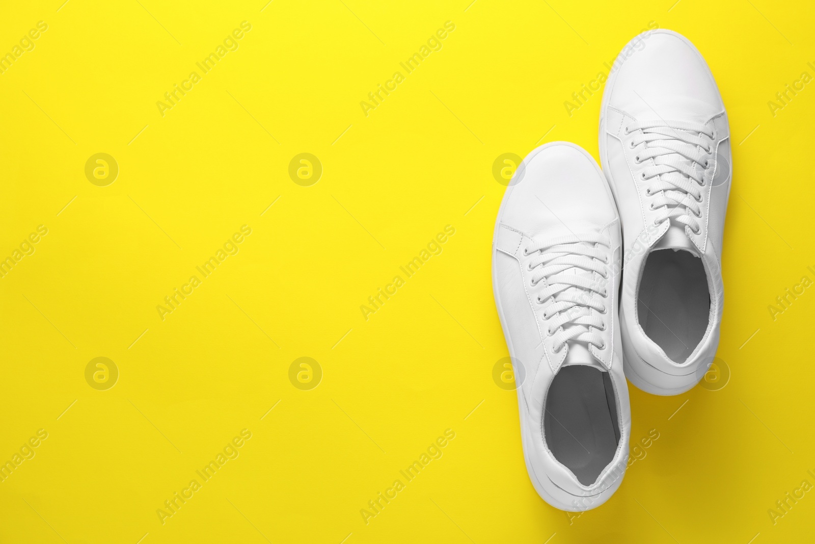 Photo of Pair of stylish white sneakers on yellow background, top view. Space for text