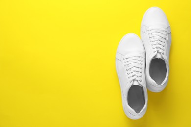 Photo of Pair of stylish white sneakers on yellow background, top view. Space for text