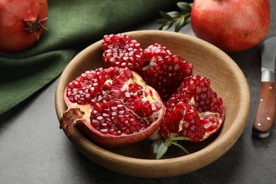 Photo of Fresh pomegranates, green leaves and knife on grey table, closeup