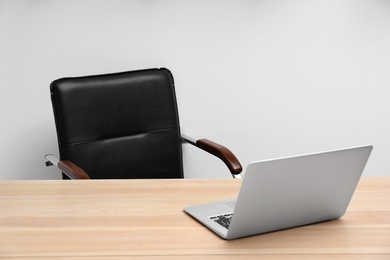 Photo of Stylish workplace interior with office chair and laptop on wooden table